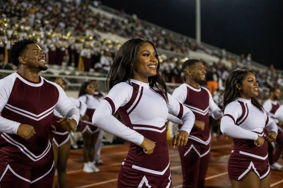 An HBCU college cheer squad cheering from the track in front of the stands at a football game