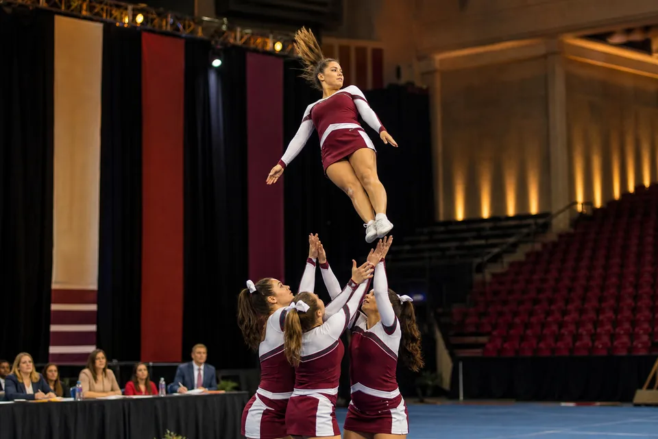 A small college competitive cheer team performing a basket toss on a spring floor at a national championship